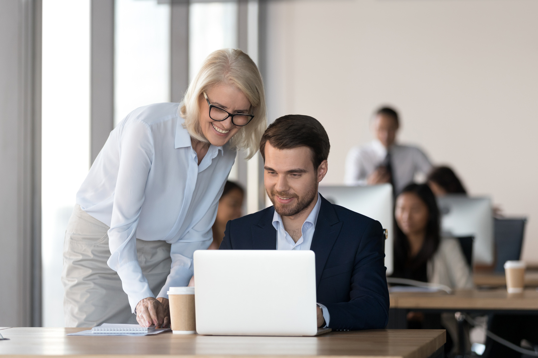 Friendly mentor training employee in office helping with computer work